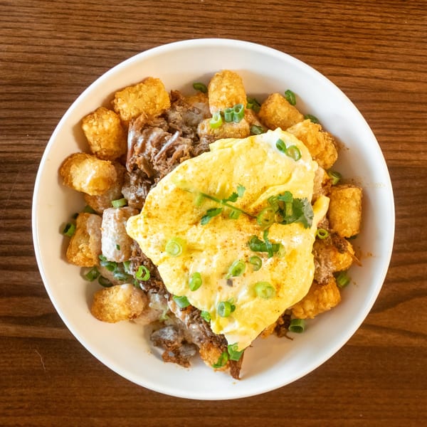 A breakfast bowl with tater tots, pulled pork, scrambled eggs, and green onions.