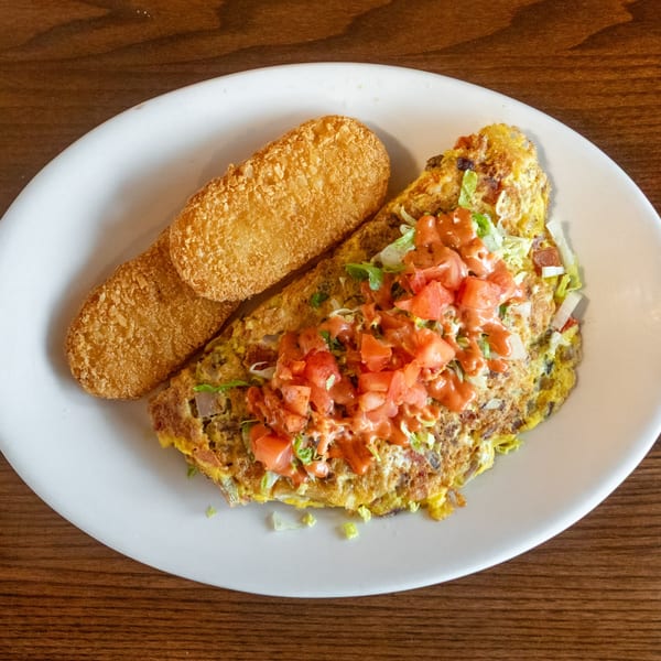 A State Street Cafe omelet topped with diced tomatoes and sauce, served with two hash browns.