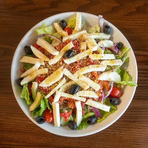 A vibrant State Street Cafe salad with lettuce, tomatoes, olives, red onion, and cheese sticks.