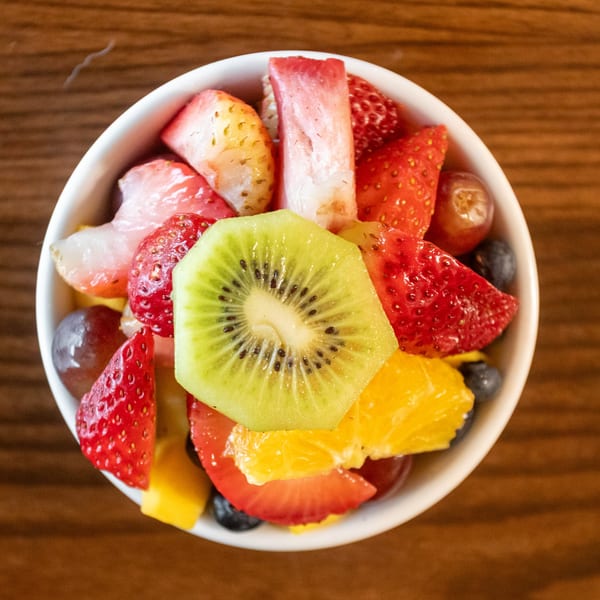 A white bowl filled with fresh fruit, including strawberries, kiwi, oranges, blueberries, and grapes.