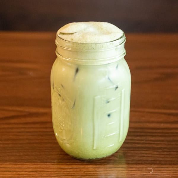 Iced matcha latte in a mason jar with foam on top, on a wooden table.