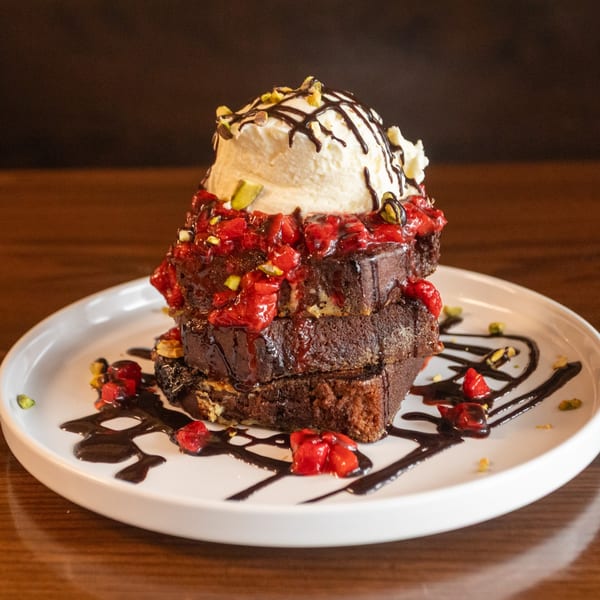 Stacked chocolate French toast with strawberries, vanilla ice cream, chocolate drizzle, and pistachios.