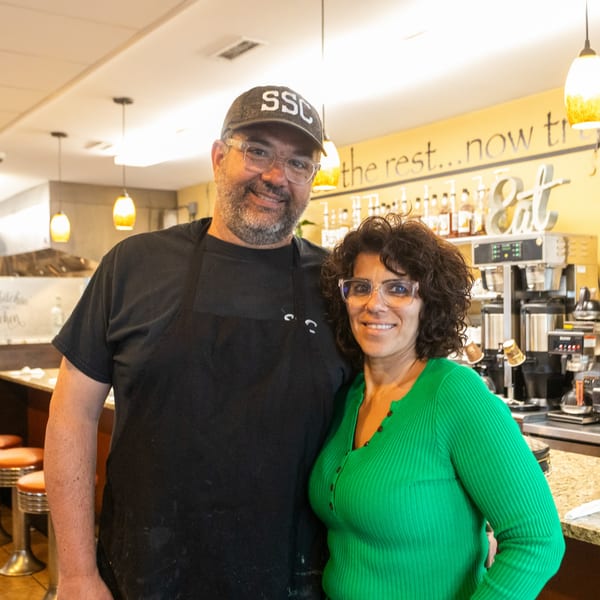 Two smiling State Street Cafe owners, a man and a woman, stand together in their cafe.