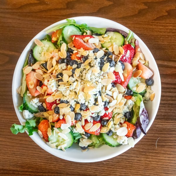 Overhead view of a State Street Cafe salad with strawberries, blueberries, cucumbers, almonds, and feta.